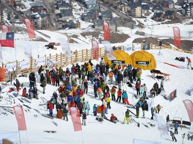 In this image there are a few people standing and sitting on the surface of the snow and a few are...