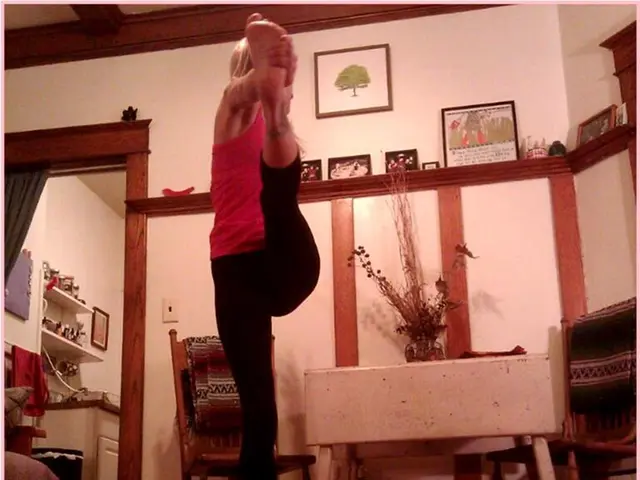 This picture is clicked inside a room. There is woman doing exercise. Behind her there is a table...