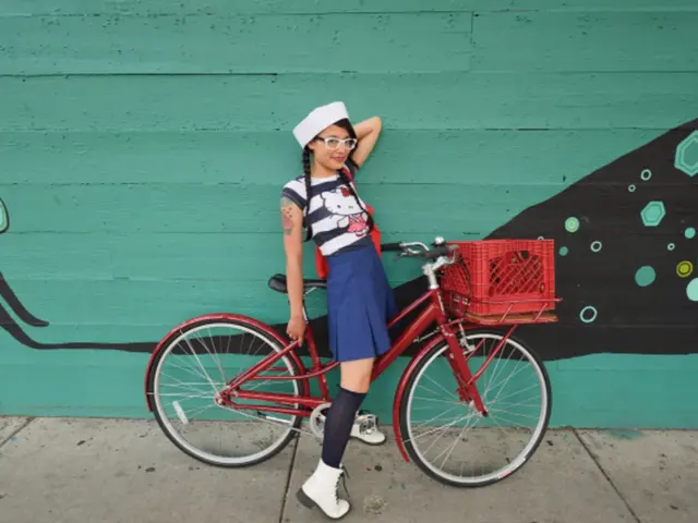 In this picture there is a girl wearing white color top and blue skirt sitting on the red color...