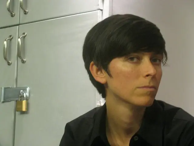 The girl in black shirt is looking at the camera and behind her, we see a white cupboard which is...