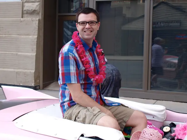 In this image in the center there is one man who is sitting and he is wearing spectacles and...