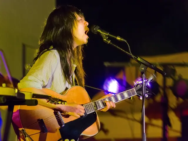 The picture is clicked in a musical concert where a lady is playing a guitar and singing with a mic...