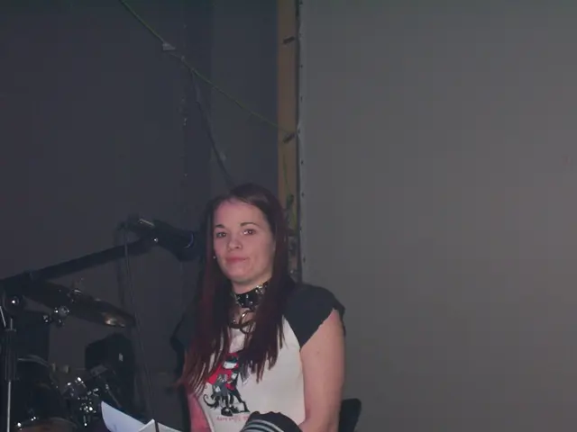 In this image we can see a woman holding papers. In the left side of the image we can see some...