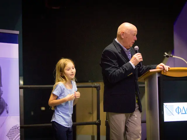 In this picture there is a man standing and holding a microphone, in front of him we can see stand...