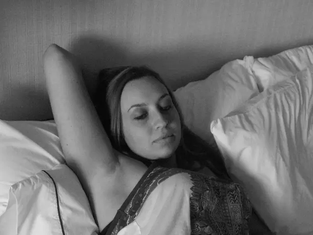 This is a black and white picture. The woman in white dress was lying on a bed. On the bed there...