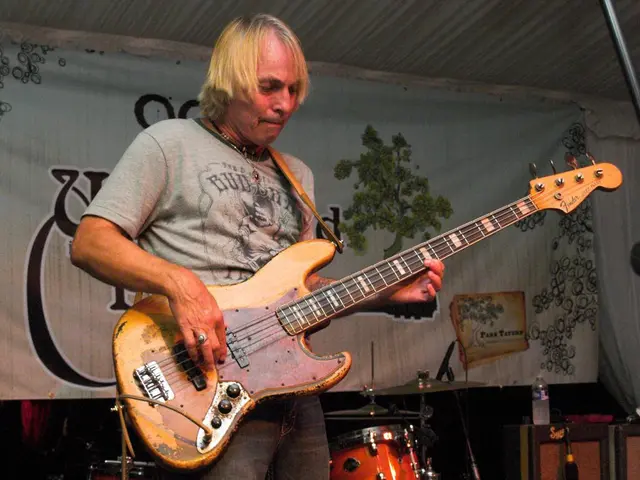In this image, there is a person standing and playing a guitar. A roof top is of tin shed. The...