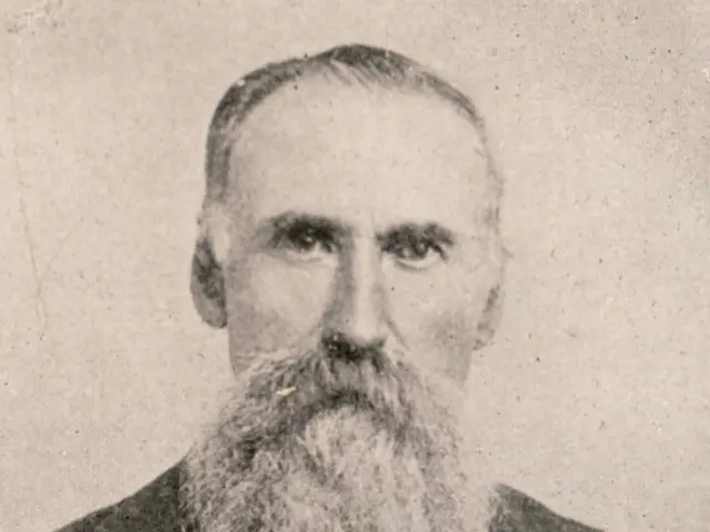 It is a black and white image. in this image we can see a person with beard.