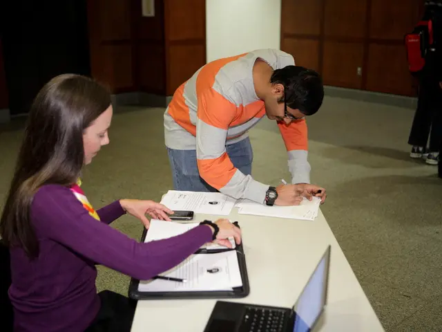 On the left side, there is a woman in a violet colored t-shirt, sitting on a chair, watching...