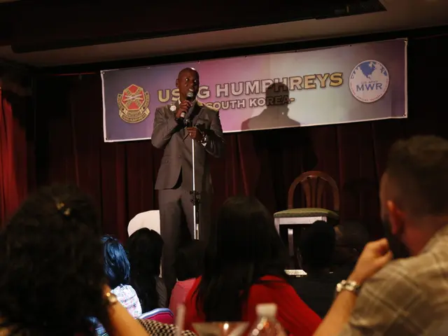 In this image we can see a person holding a microphone, on the stage which a contains a chair, a...