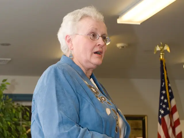 In the image there is a woman and talking on the right side there is a flag and on the left side...