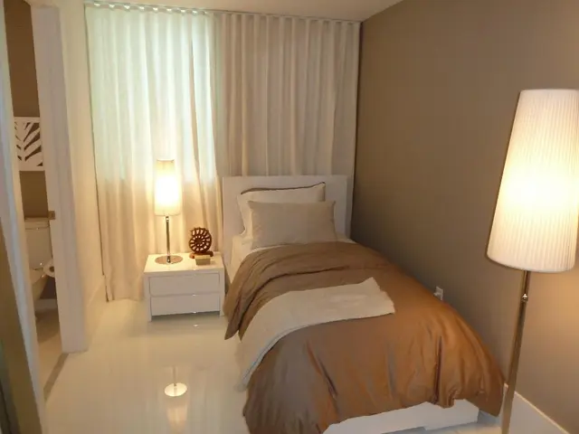 This picture shows the inner view of a room. There are two pillows, one towel, one bed, one bedside...