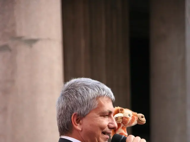 In this image their is a man who is holding a mic with his right hand and speaking. At the...