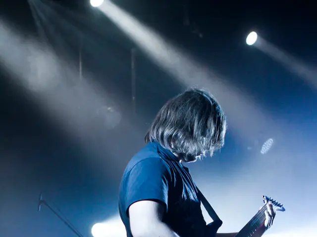 In this image I can see a person standing on the stage and playing musical instrument, behind him...