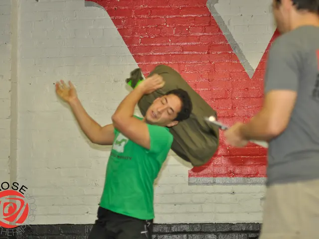 This image consists of two persons. In the front, the man wearing green T-shirt is holding a bag....