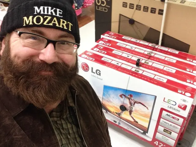 In front of the image there is a person with a smile on his face, behind him there are televisions...