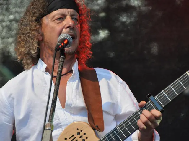 In this picture there is a man who is singing a song, there is a mike in front of him he is wearing...