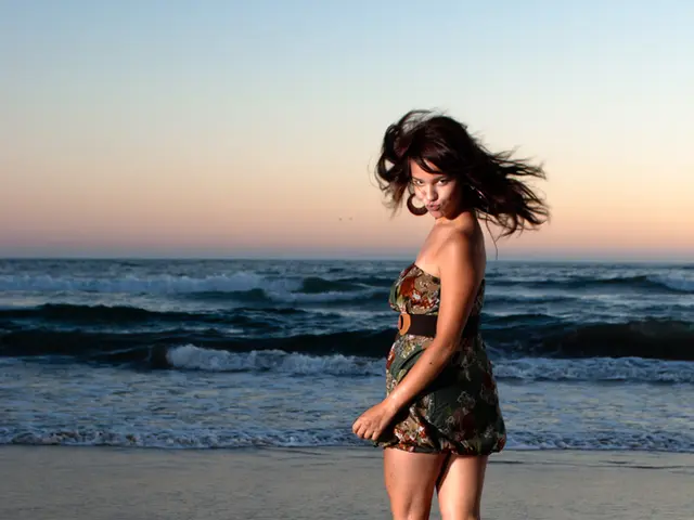 In this picture we can see a girl standing on the beach and giving a pose to the camera. Behind...