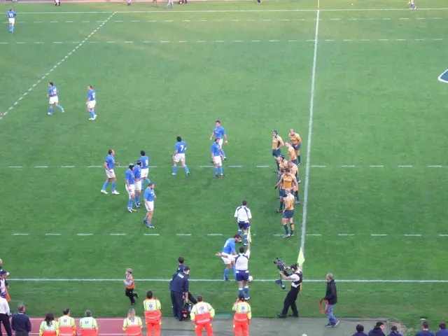 In this image we can see a few people, some of them are on the football ground, a person is holding...