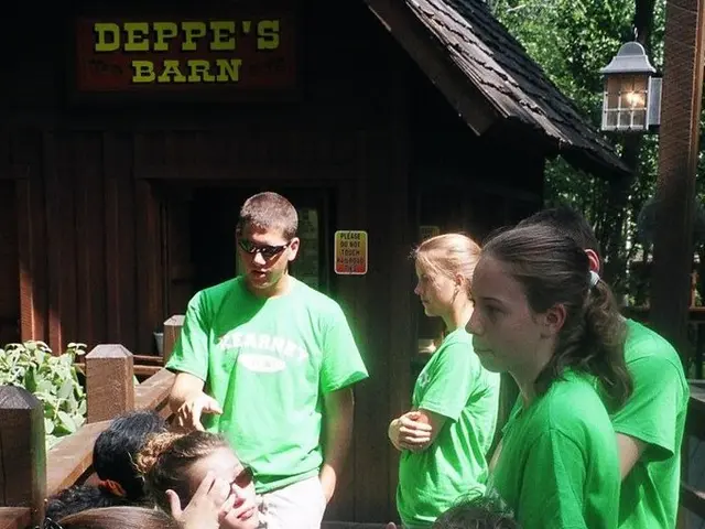 In this image there are few people wearing green t-shirt. Few are sitting few are standing. In the...