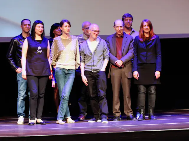 In the foreground I can see a group of people are standing on the stage. In the background I can...