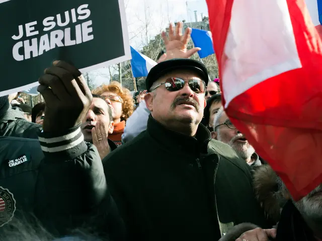 In this image there are people protesting on a road, holding flags, posters in their hands, in the...