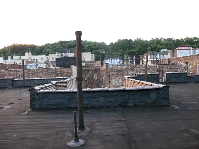 In this picture I can see buildings and few poles and I can see trees and a cloudy sky.