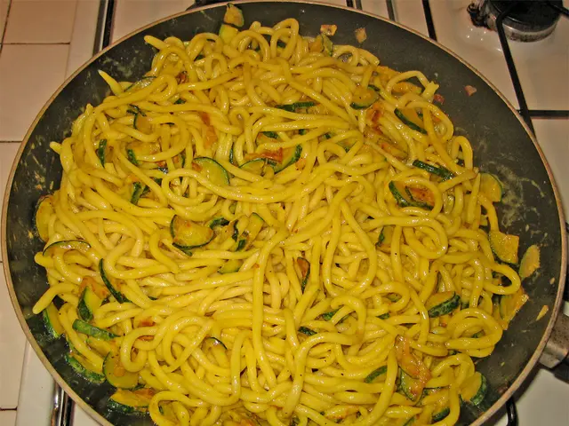 In this image there is a pan on the stove. In the pan there are noodles.