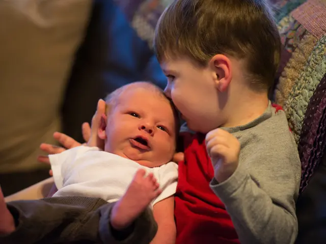 In this image I can see the kid is holding the baby and they are wearing different color dresses....