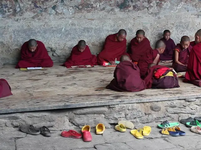 In the image there are many buddhist monks sitting on wooden floor reading books and in the front...