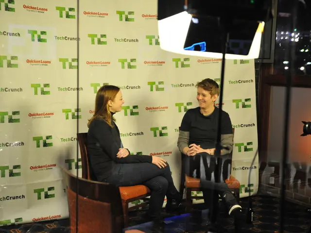 In the image we can see a girl and a boy sitting on chair talking to each other. This is a camera.