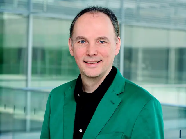 This image consists of a man wearing a green suit. In the background, we can see a glass and a...