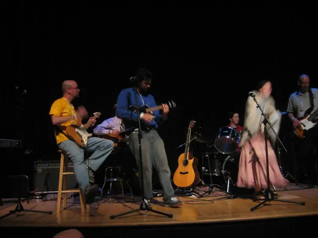 There is a music band standing on the stage. In the background there is a person playing drums. In...