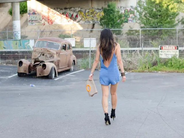 In the image we can see there is a woman walking on the road and she is holding purse in her hand....