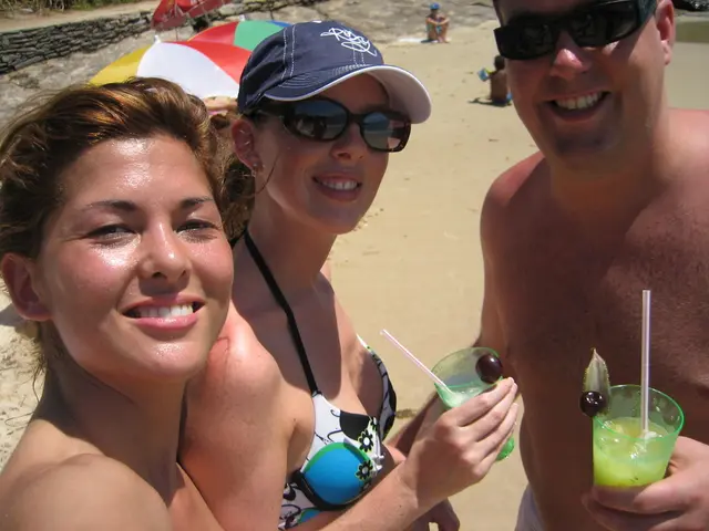 The picture is taken in a beach. In the foreground of the picture there are two women and a man,...