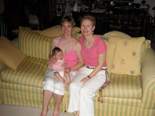 Two women are sitting on the sofa. On the left a woman is carrying a child. Behind them there are...