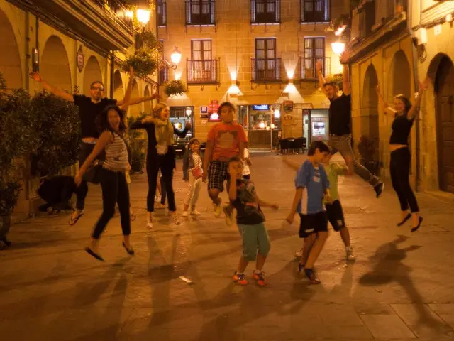 In the foreground of this image, there are persons jumping on the pavement. In the background,...