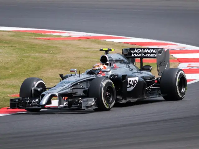 In the image there is a racing car on an empty road and behind that car there is a grass surface.