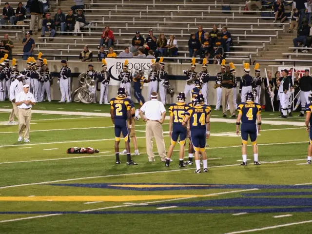 In the image there are few players and coaches were standing on the ground and in front of them, a...