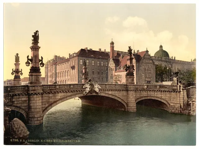 In this image there is a bridge, water, sculptures, buildings, lights, trees, sky and a watermark...