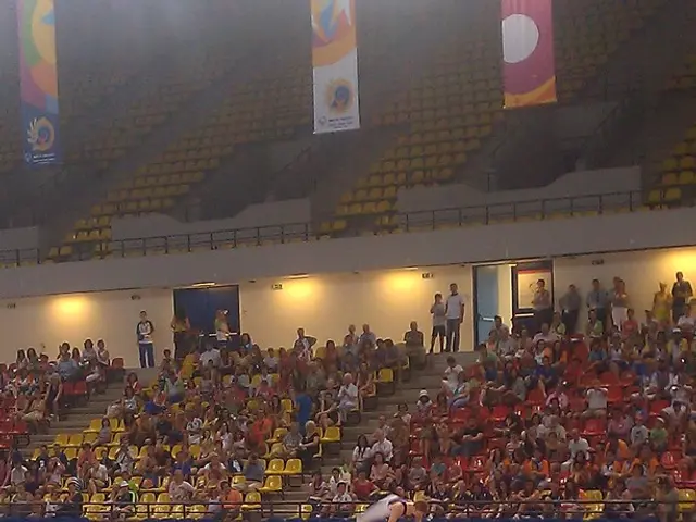 In this picture we can see a stadium, there are some people sitting on chairs, in the background...