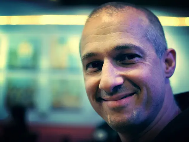 This image consists of a man wearing black dress is laughing. In the background, there are lights....