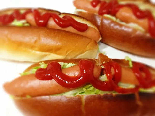 In this picture we can see hot-dogs and sauce on them.