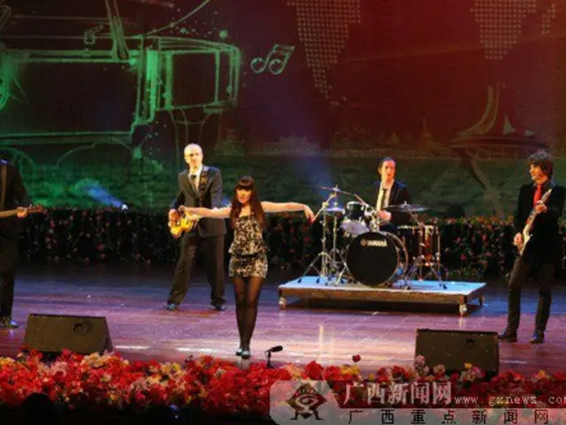 In this picture there is a woman standing on the dais, there are four men in the back and one of...