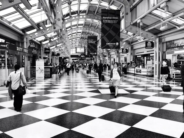 In this image I can see inside of the building in which some people are holding bags and walking,...