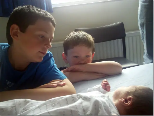 At the bottom of this image there is a baby laying. On the left side there are two boys looking at...