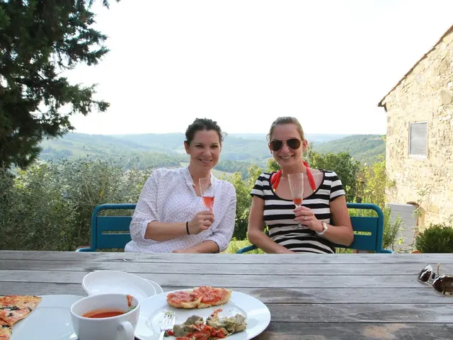 On the background we can see sky, hills trees. This is a house. Here we can see two women sitting...