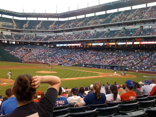 In this image we can see a stadium, few people are sitting on the chairs and few people are playing...