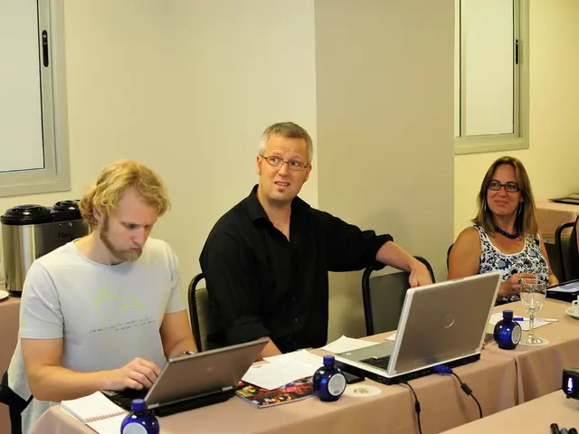 This is an inside view of a room. Here I can see two men and two women are sitting on the chairs in...