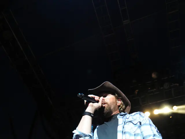 In this image the man is standing on the stage and singing the song using a mic in his hand and he...