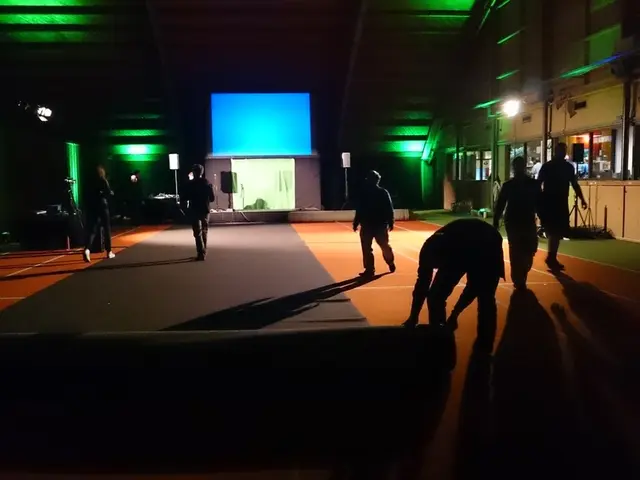 In this image, we can see a dark room, there is carpet on the floor, there are some people walking...